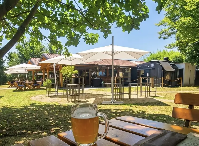 Dehors di Agri-K con ombrelloni bianchi, tavoli in legno e boccale di birra in primo piano